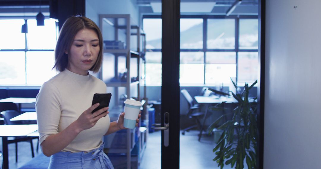 Young Woman Walking in Office While Looking at Smartphone and Holding Coffee Cup - Free Images, Stock Photos and Pictures on Pikwizard.com