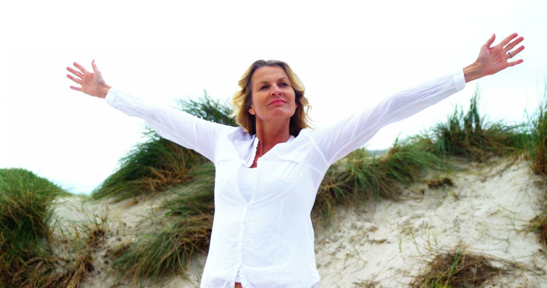 Joyful Mature Woman with Arms Outstretched on Beach Dune - Free Images, Stock Photos and Pictures on Pikwizard.com