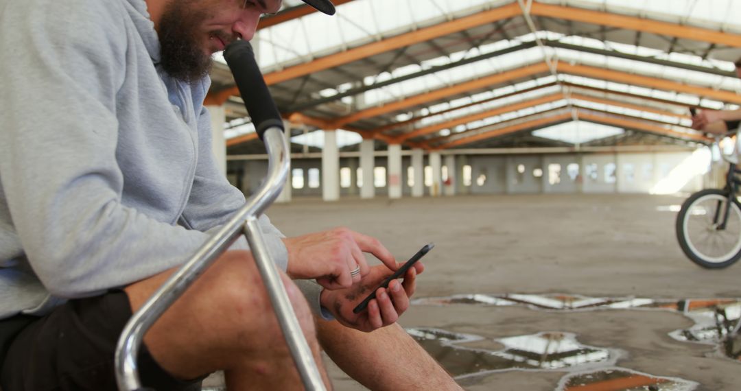 BMX Rider Taking Break in Abandoned Warehouse, Using Smartphone - Free Images, Stock Photos and Pictures on Pikwizard.com