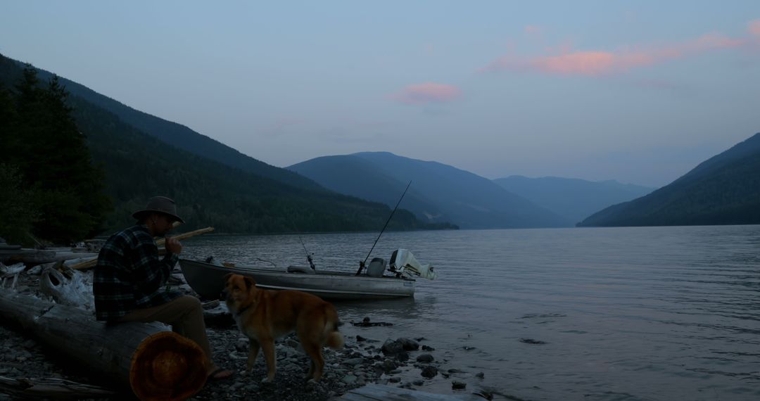 Man playing flute by peaceful lakeside with dog at sunset - Free Images, Stock Photos and Pictures on Pikwizard.com