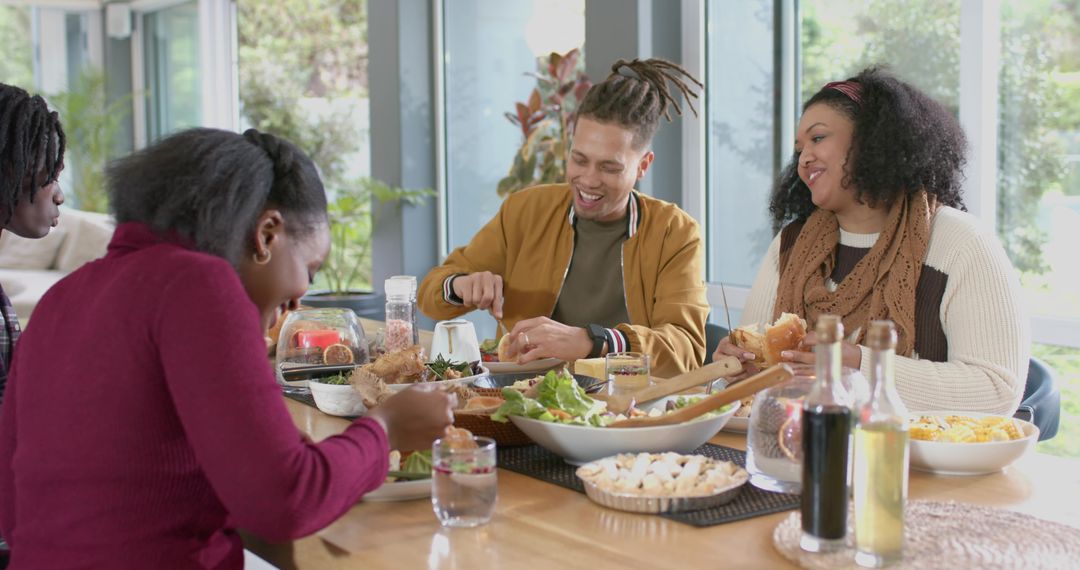 Multiracial friends sharing salad and laughing at sunlit wooden dining table