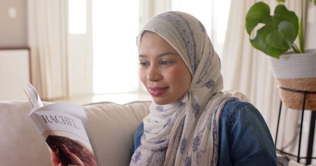 Smiling Muslim Woman Wearing Hijab Reading Book at Home - Free Images, Stock Photos and Pictures on Pikwizard.com