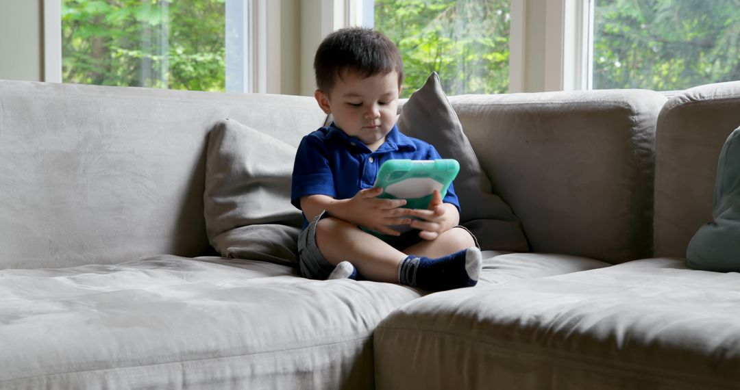 Young Child Playing with Tablet on Sofa - Free Images, Stock Photos and Pictures on Pikwizard.com