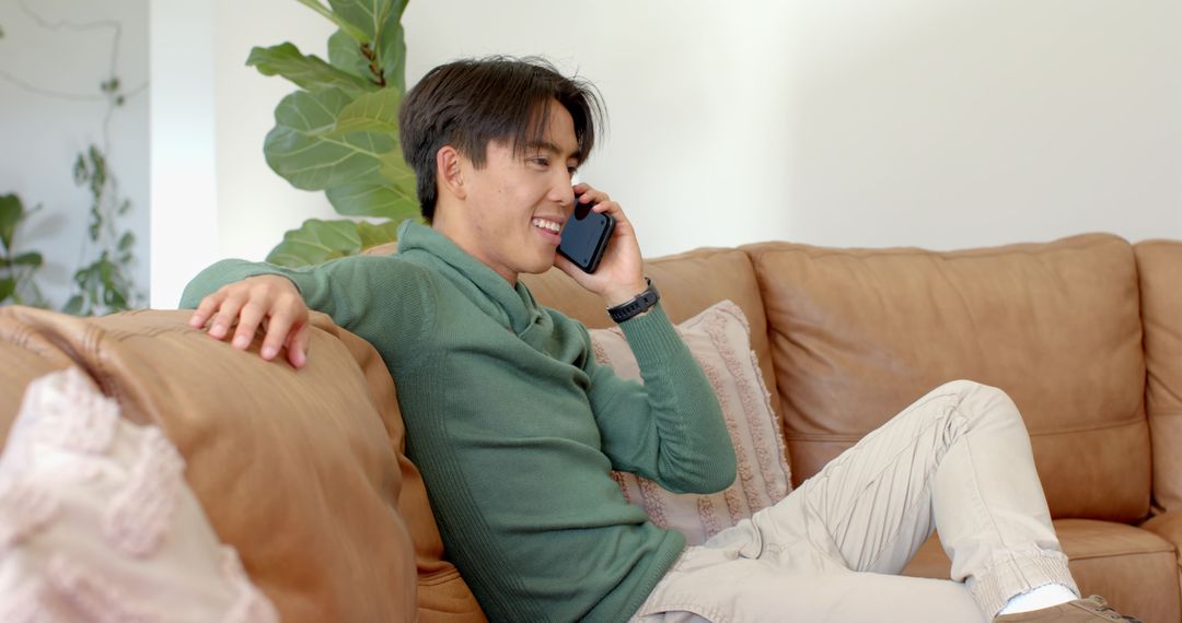 Asian Man Relaxing on Sofa Checking Smartphone at Home