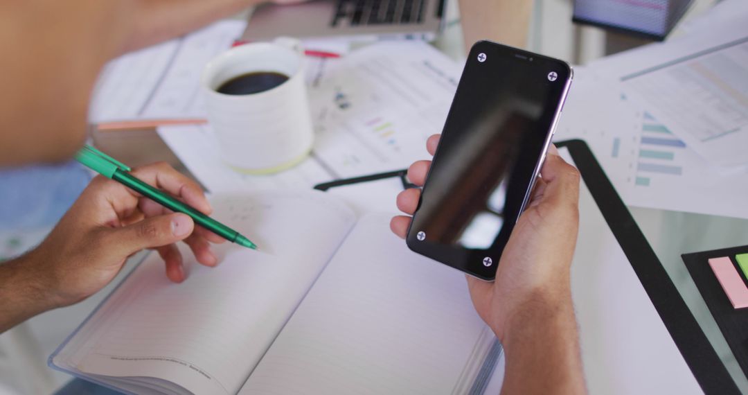 Person Using Smartphone and Writing in Notebook at Home Office