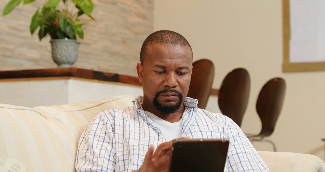 African American man focused on his tablet at home - Free Images, Stock Photos and Pictures on Pikwizard.com