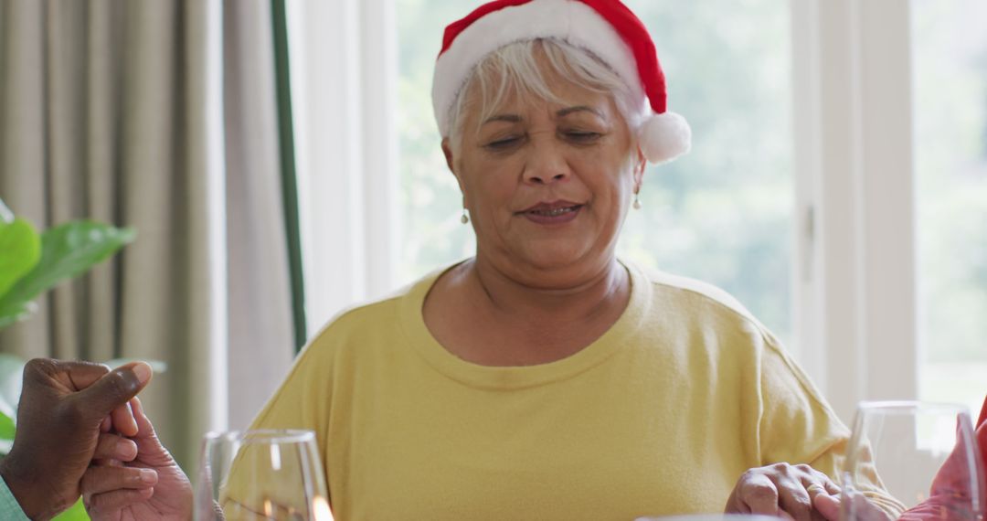 Elderly Woman Wearing Santa Hat Praying During Christmas Meal - Free Images, Stock Photos and Pictures on Pikwizard.com