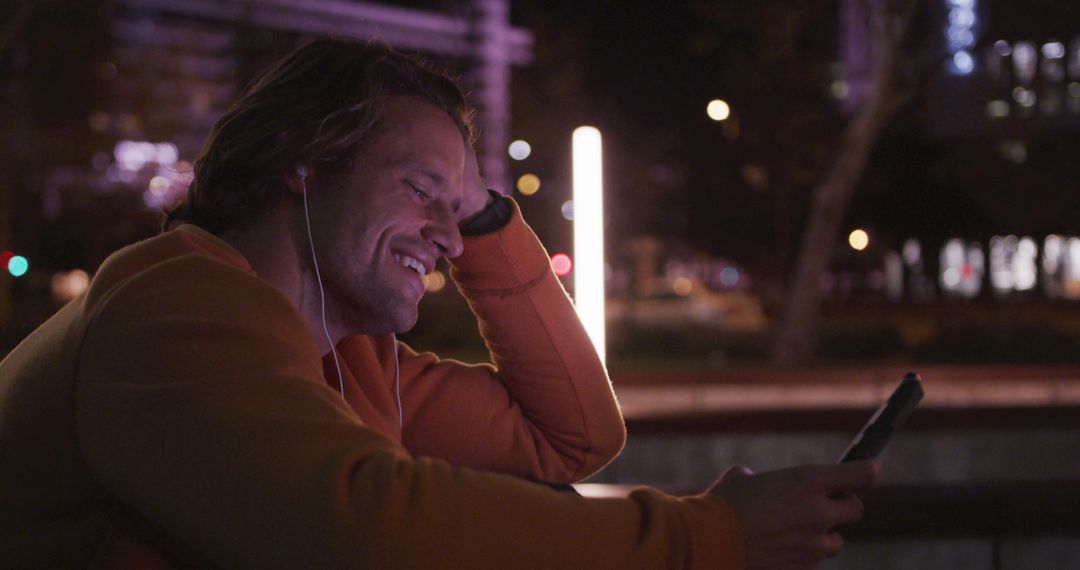 Man Smiling at Night While Using Smartphone with Earbuds - Free Images, Stock Photos and Pictures on Pikwizard.com