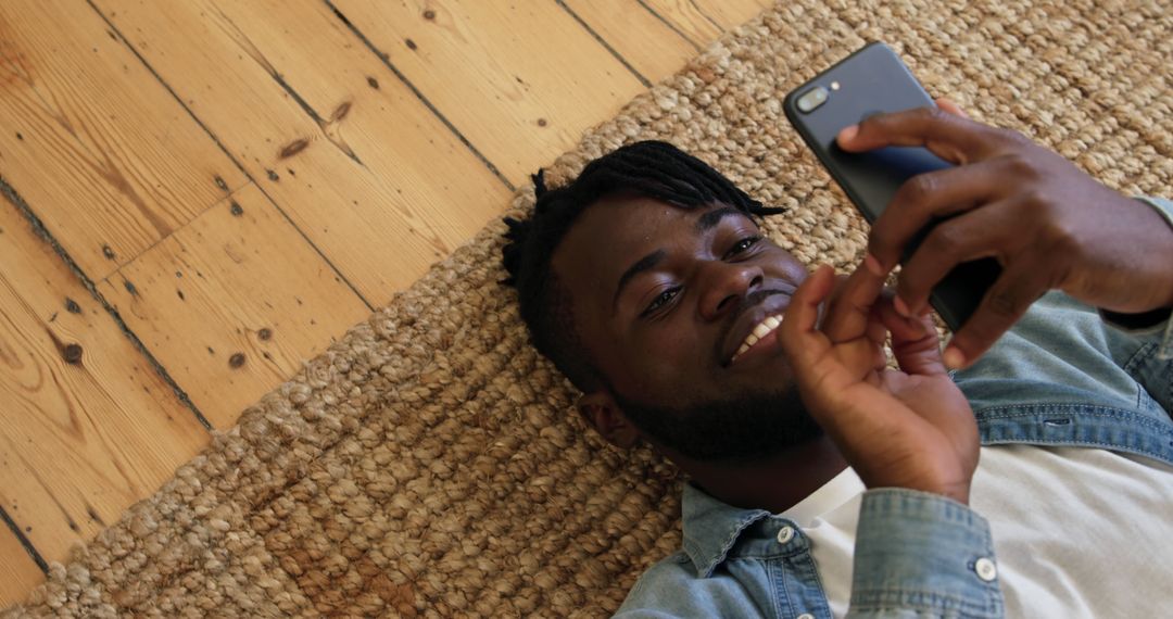 Man smiling while using smartphone on wooden floor - Free Images, Stock Photos and Pictures on Pikwizard.com