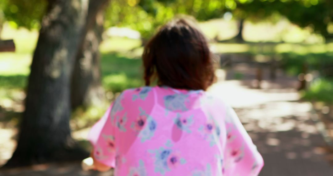 Woman Walking Outdoors in Pink Floral Shirt in Sunlit Park - Free Images, Stock Photos and Pictures on Pikwizard.com