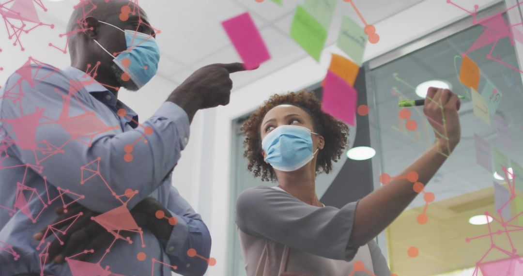 Collaborating on glass wall with sticky notes and masks during team brainstorming session
