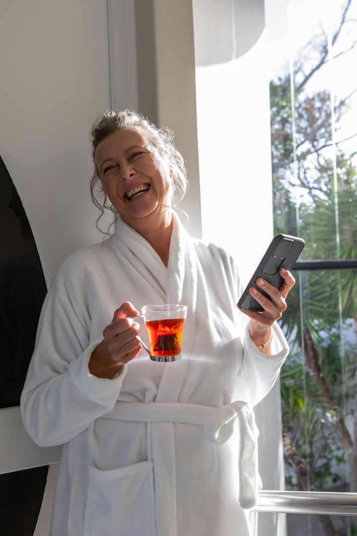 Senior Woman Relaxing with Tea in Bathrobe on Sunny Balcony