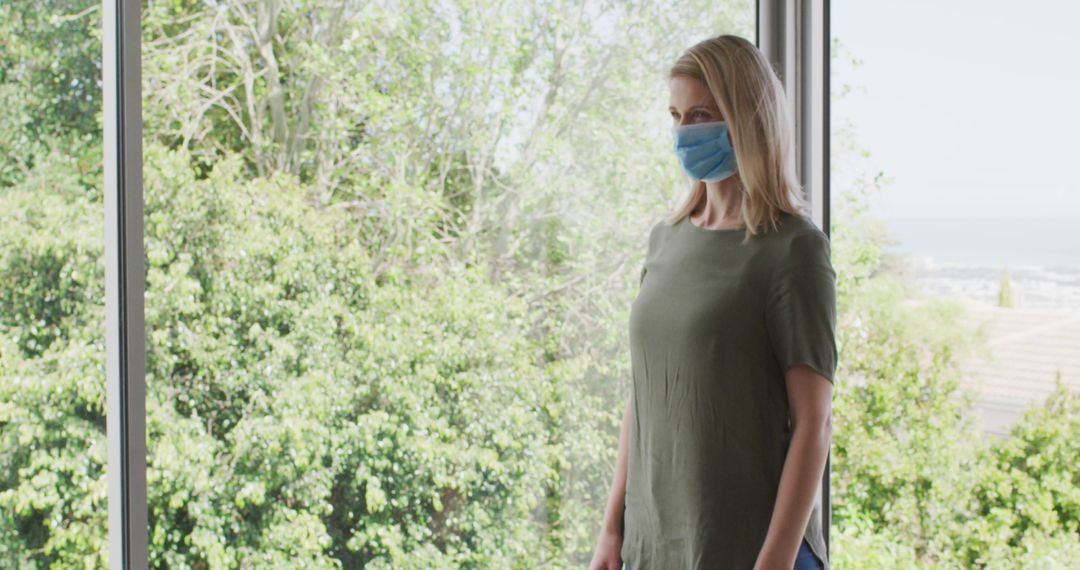 Woman Wearing Face Mask Standing by Window, Green Outdoor View - Free Images, Stock Photos and Pictures on Pikwizard.com