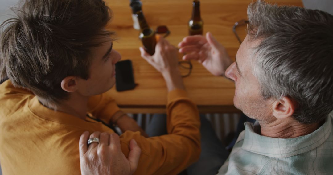 Young Man and Older Man Discussing Over Beers at Wooden Table - Free Images, Stock Photos and Pictures on Pikwizard.com