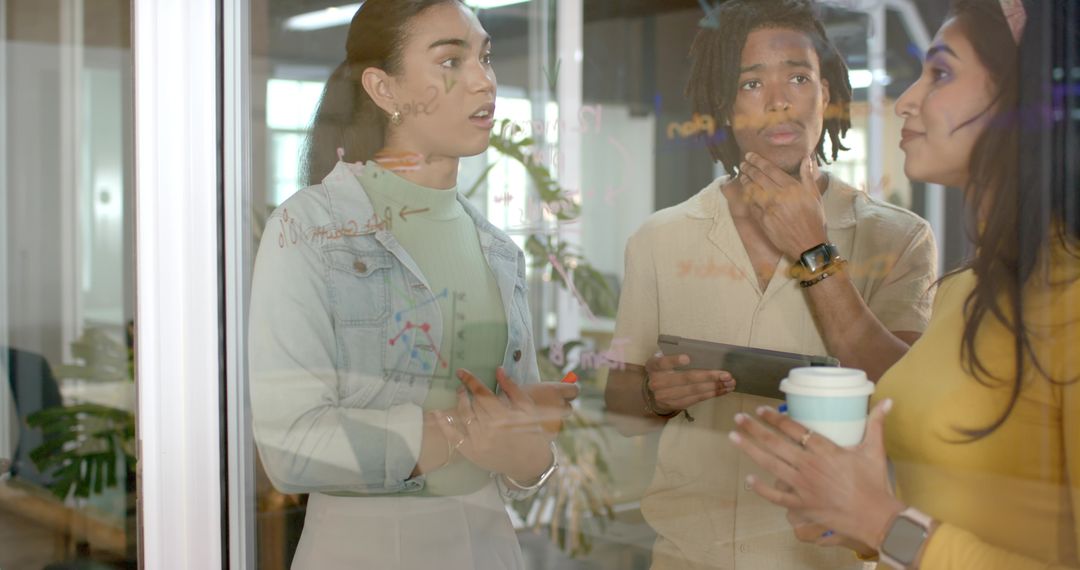 Diverse team collaborating at glass wall with diagrams, tablet and coffee for planning