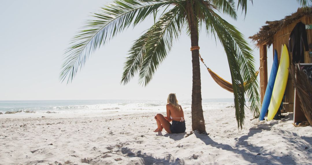 Woman Relaxing on a Tropical Beach near Surfboards and a Palm Tree - Free Images, Stock Photos and Pictures on Pikwizard.com