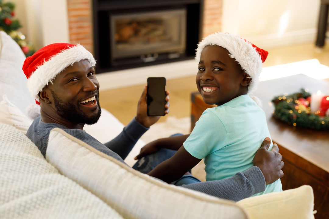 Father and son in Santa hats smile and take a selfie on the couch. - Free Images, Stock Photos and Pictures on Pikwizard.com