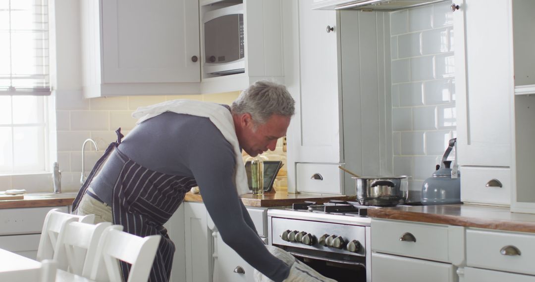 Happy caucasian man wearing apron, standing in kitchen, cooking dinner - Free Images, Stock Photos and Pictures on Pikwizard.com