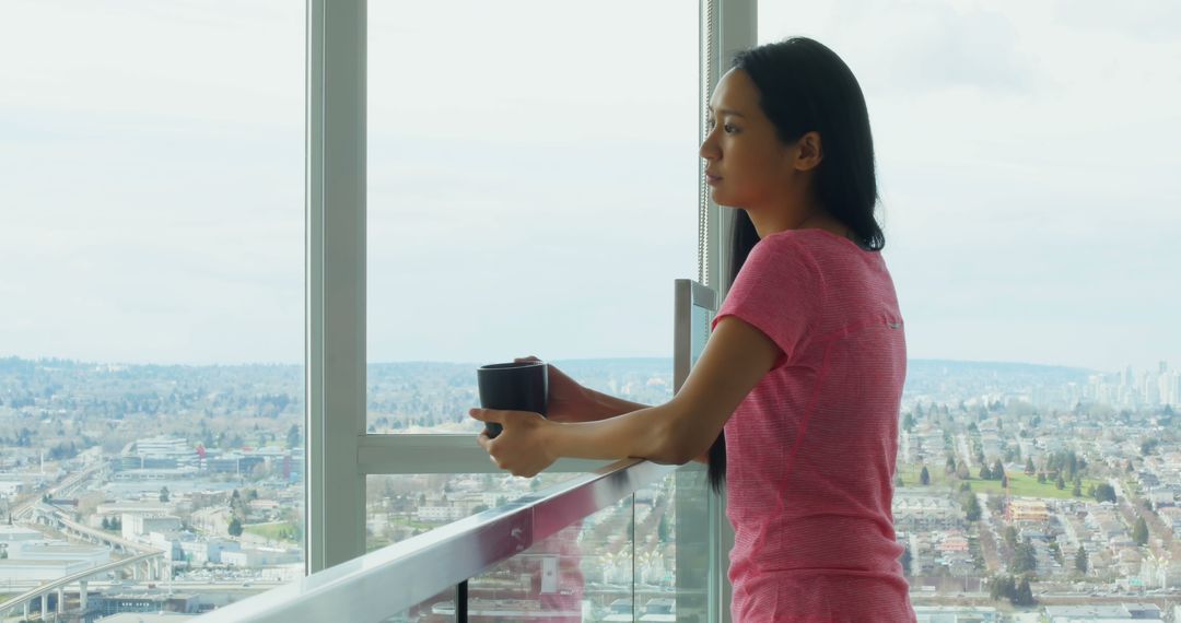 Woman Standing by Window Holding Cup Overlooking Cityscape - Free Images, Stock Photos and Pictures on Pikwizard.com