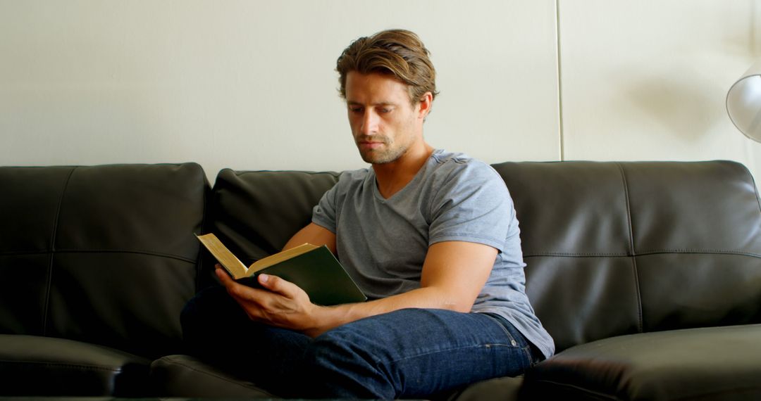 Young Man Relaxing on Couch Reading Book - Free Images, Stock Photos and Pictures on Pikwizard.com