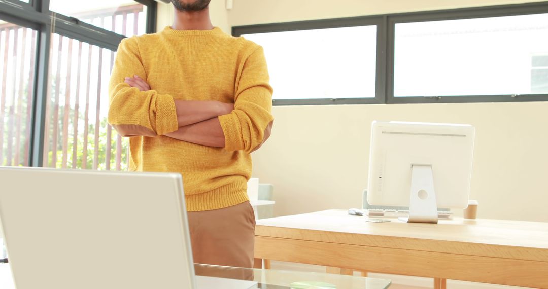 Man Standing in Bright Modern Office with Folded Arms in Yellow Sweater - Free Images, Stock Photos and Pictures on Pikwizard.com