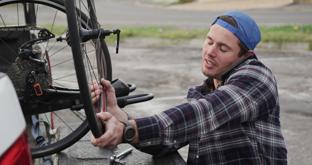 Man Fixing Bicycle Wheel While Talking on Phone Outdoors - Free Images, Stock Photos and Pictures on Pikwizard.com