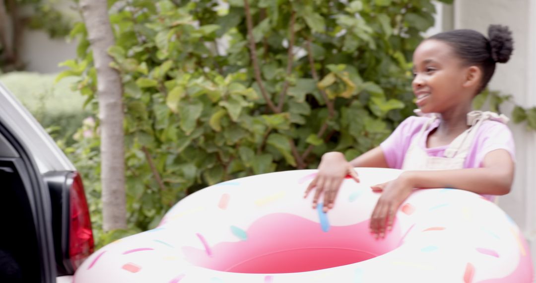 Smiling Girl Holding Pink Doughnut Pool Float in Driveway