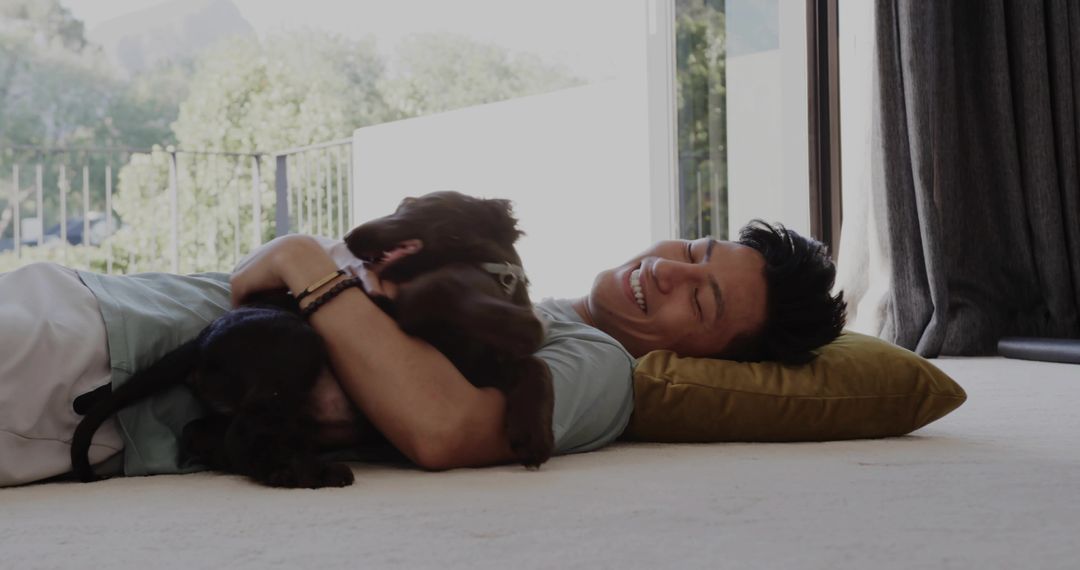 Smiling man lying on carpet hugging brown dog while resting on mustard pillow