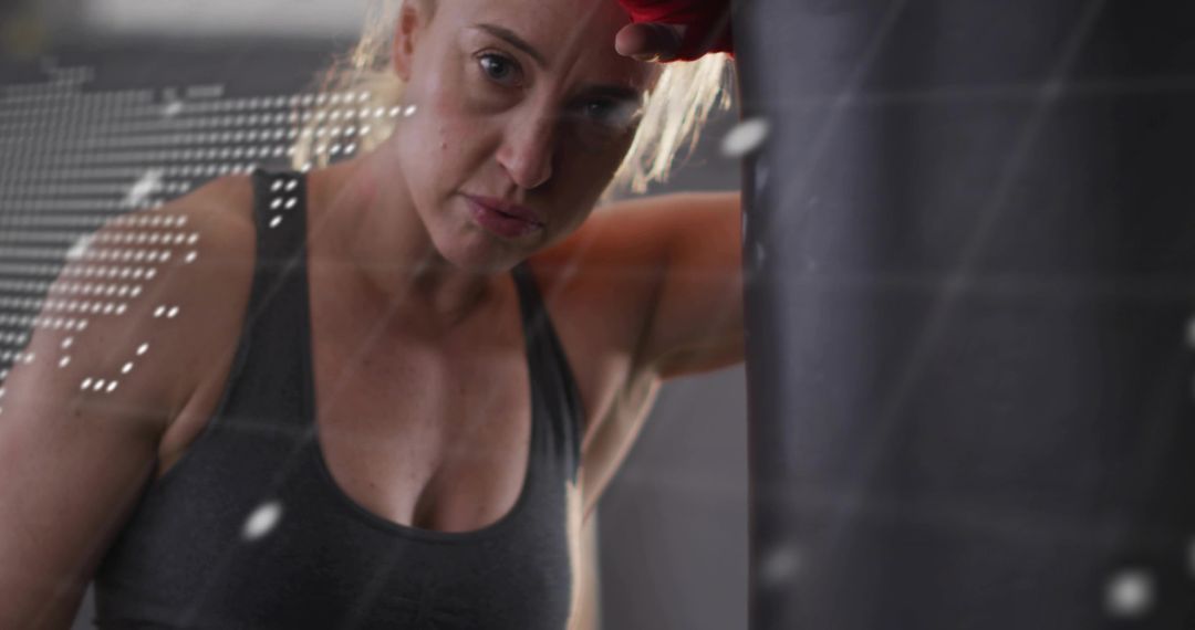 Leaning woman resting at punching bag after intense boxing session, focused determination