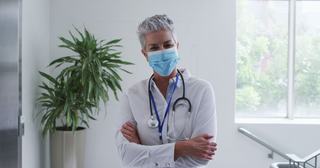 Portrait of caucasian female senior doctor wearing face mask standing with arms crossed in hospital - Free Images, Stock Photos and Pictures on Pikwizard.com