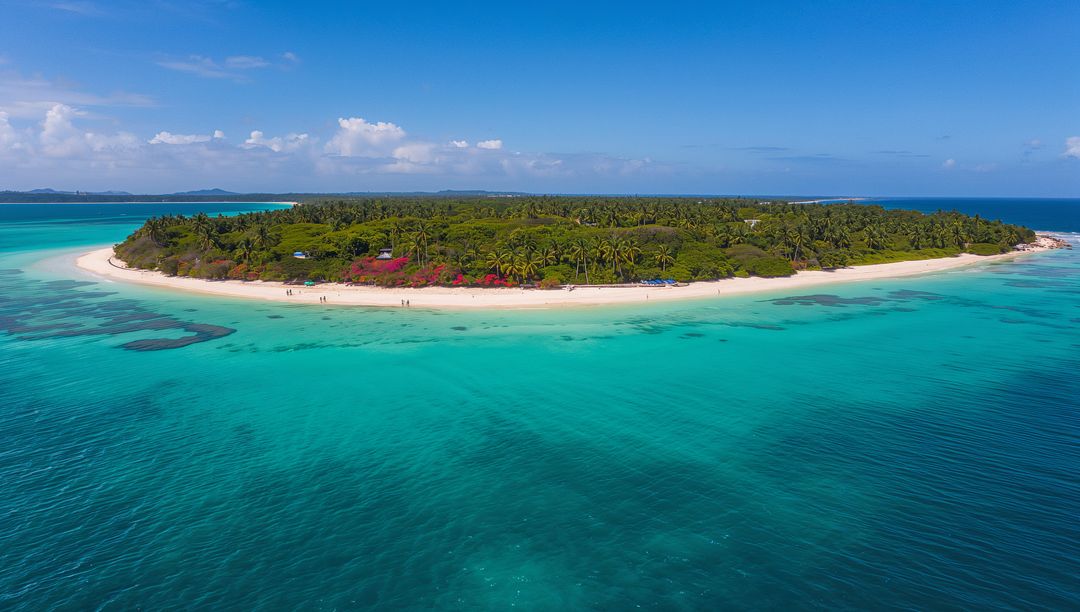 Aerial overlooking tropical islet with white sand beach and turquoise lagoon
