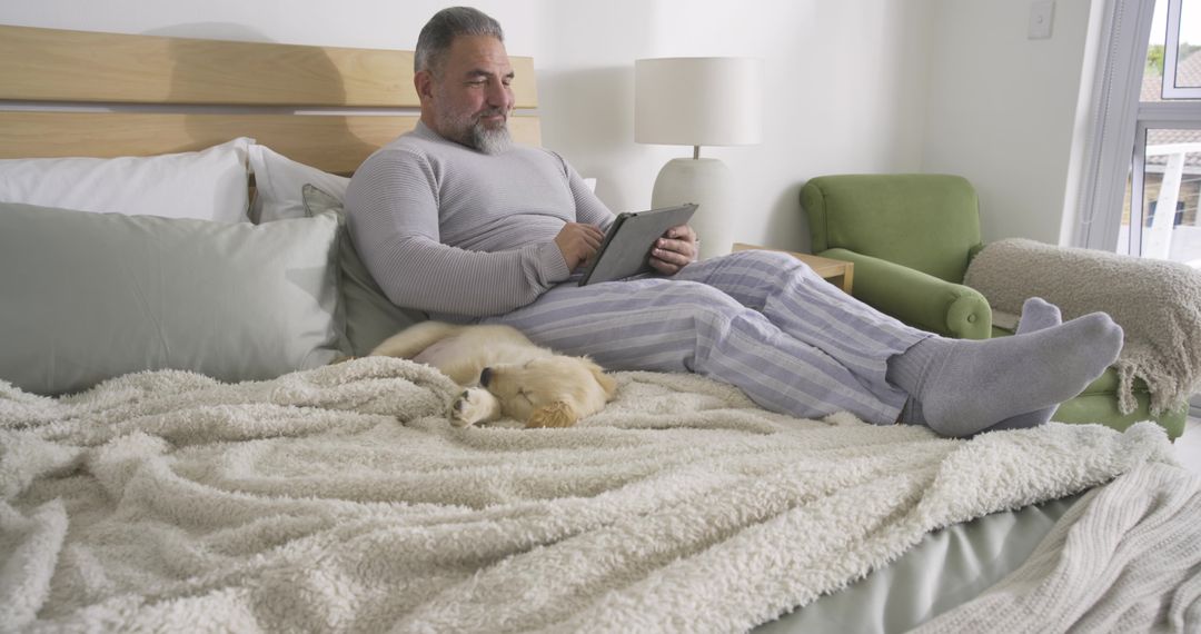 Middle-aged Man Relaxing with Tablet and Sleeping Puppy in Cozy Bedroom
