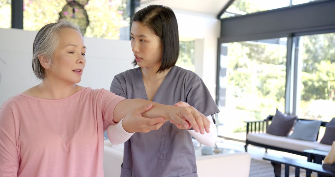 Physiotherapist Assists Senior Asian Woman with Arm Exercises