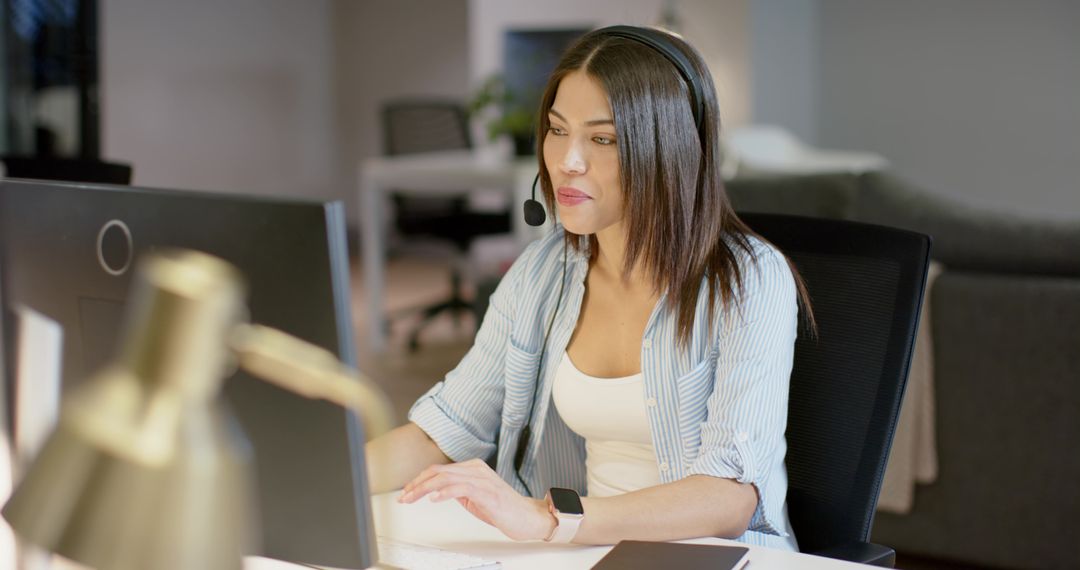 Indian woman working remotely with headset at modern home office desk typing on keyboard