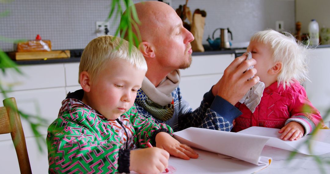 Father Caring for Daughter While Son Draws on Table at Home