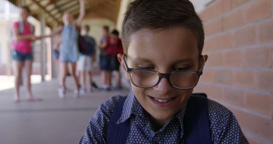 Smiling Caucasian Schoolboy in Glasses Sitting in School Hallway