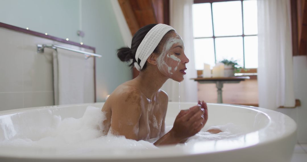 Biracial woman sitting in bathtub taking a bath, cleaning her face - Free Images, Stock Photos and Pictures on Pikwizard.com