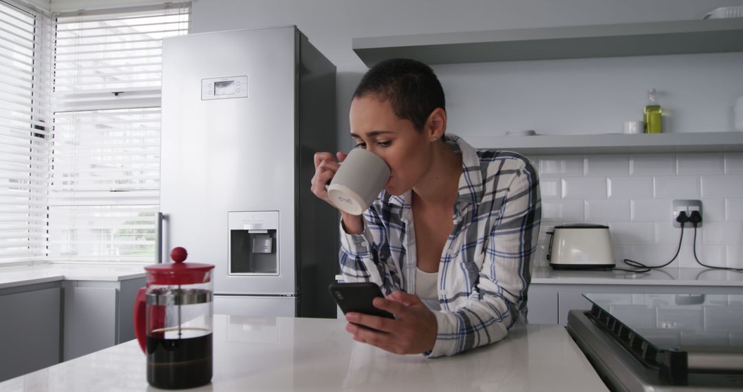 Woman Enjoying Coffee and Browsing Smartphone in Modern Kitchen - Free Images, Stock Photos and Pictures on Pikwizard.com