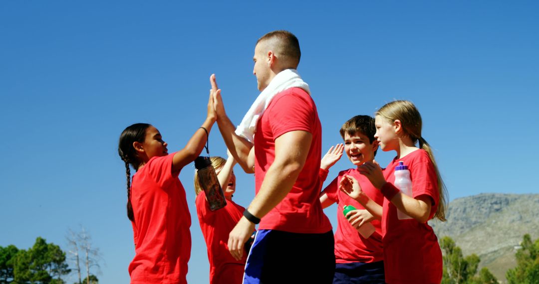 Coach Giving High Fives to Enthusiastic Kids During Outdoor Sports Event - Free Images, Stock Photos and Pictures on Pikwizard.com