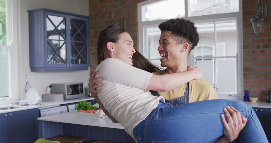 Happy biracial couple embracing and laughing together in kitchen - Free Images, Stock Photos and Pictures on Pikwizard.com
