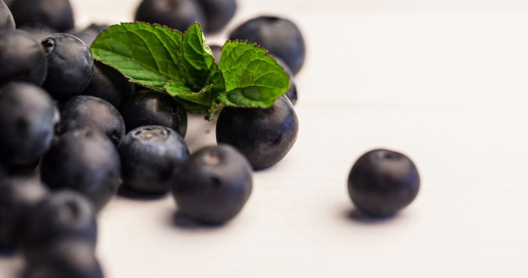 Fresh Blueberries with Mint Leaves on White Surface
