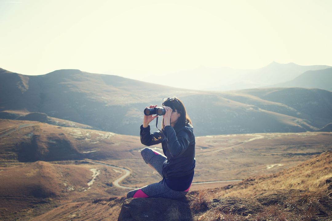 Woman Wearing Black Jacket Using Binoculars Sitting on Mountain - Free Images, Stock Photos and Pictures on Pikwizard.com