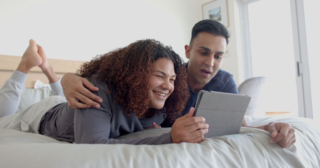 Smiling Mixed Race Couple Enjoying Digital Tablet Together in Cozy Bedroom - Free Images, Stock Photos and Pictures on Pikwizard.com