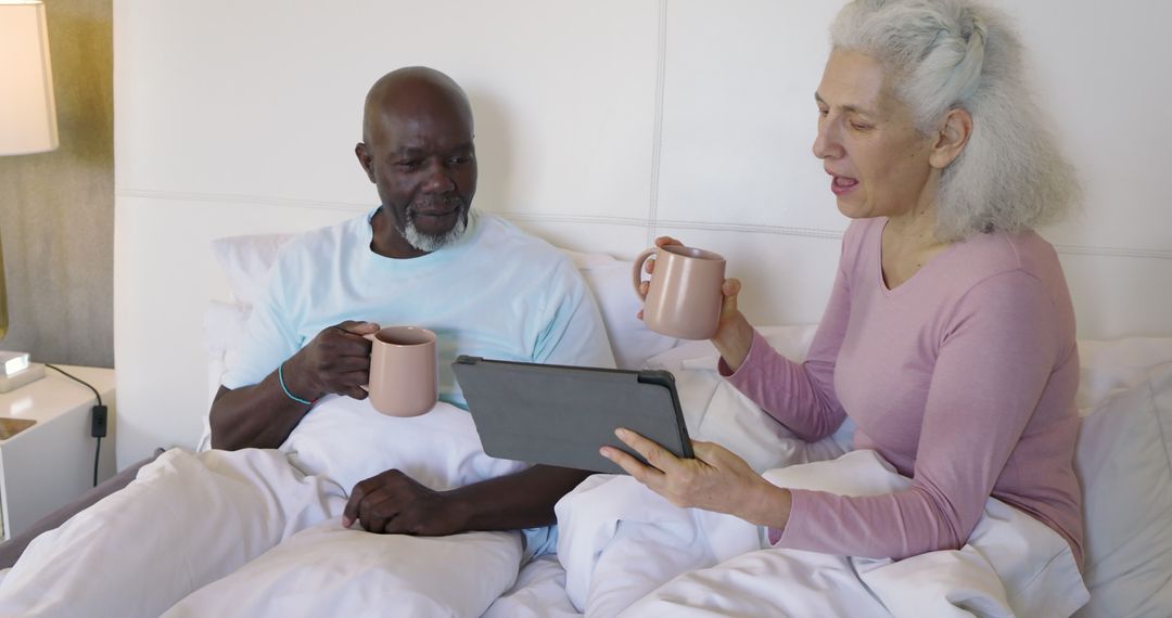 Senior Couple Drinking Coffee and Using Tablet in Bed