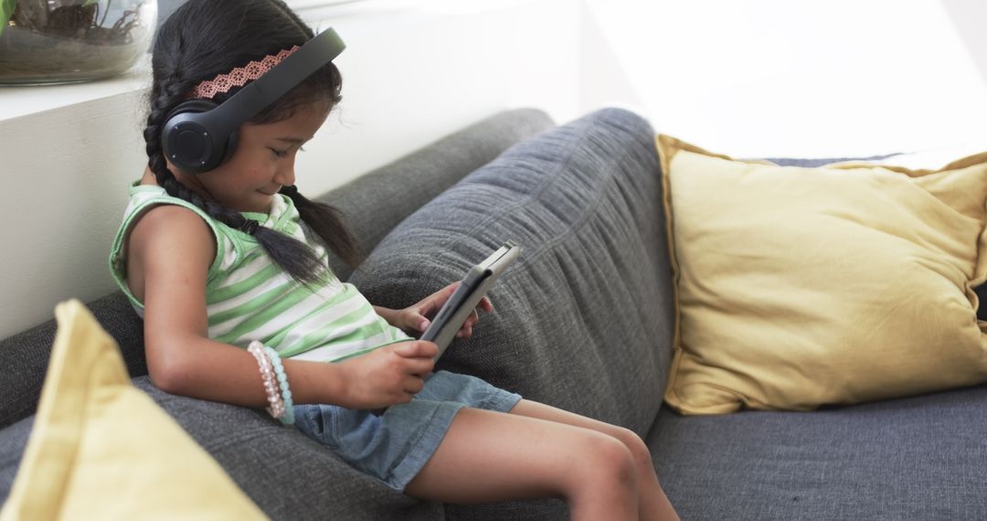 Girl with Headphones Using Tablet on Couch in Relaxed Atmosphere