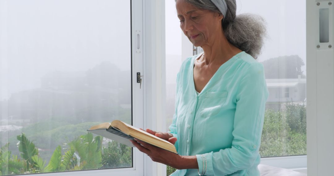 Senior Woman Reading Near Window in Tranquil Home Environment - Free Images, Stock Photos and Pictures on Pikwizard.com