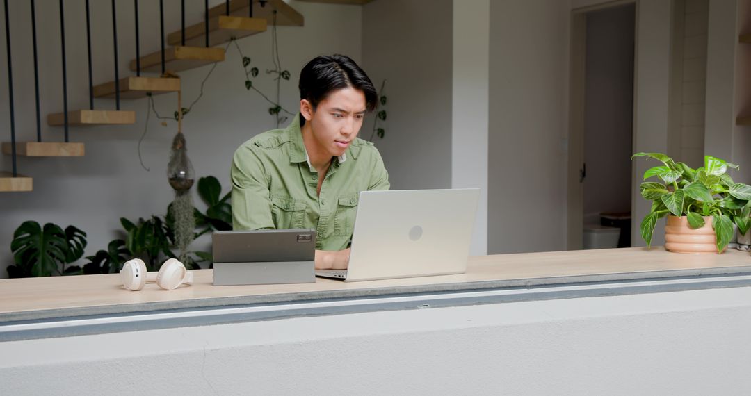 Man Typing on Laptop at Home Counter with Greenery and Modern Decor