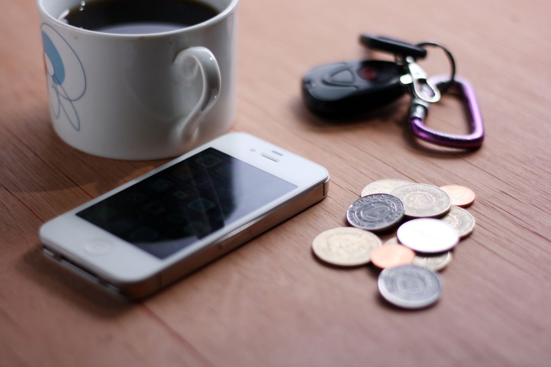 Essentials on Wooden Table with Coffee, Smartphone, Money, and Keys