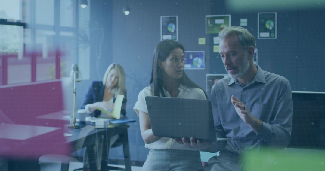 Two professionals collaborating over laptop in modern glass-walled office with charts
