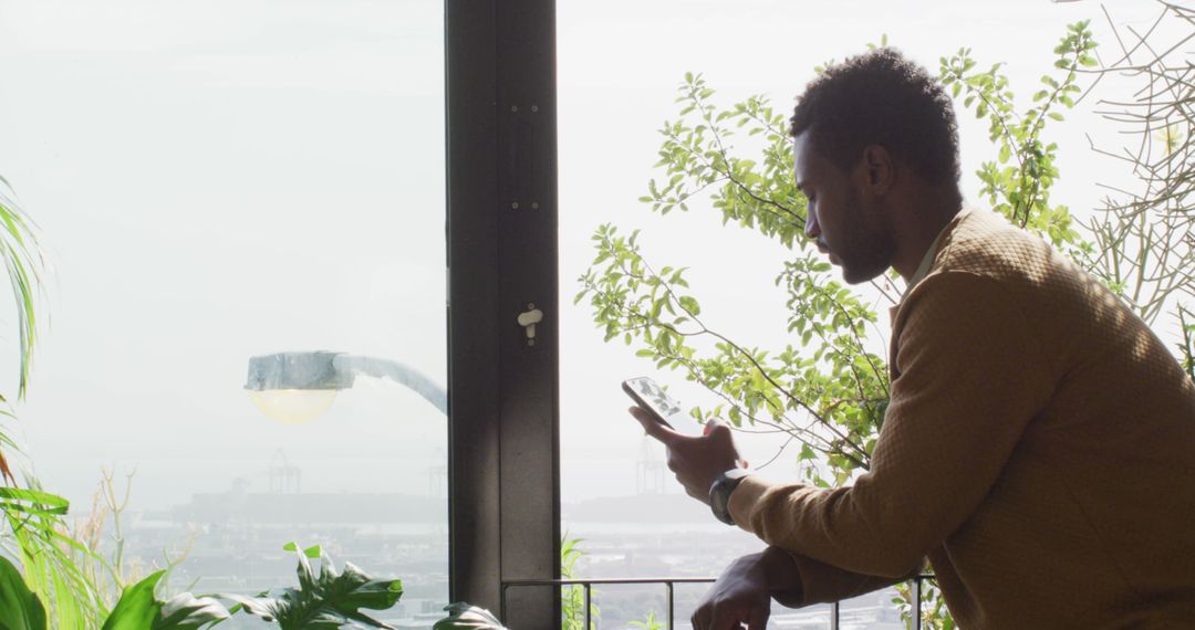 Man Relaxing with Smartphone Near Large Window in Natural Setting